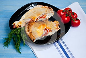 Closed calzone pizza on a wooden table with fresh tomatoes and d