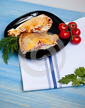 Closed calzone pizza on a wooden table with fresh tomatoes and d