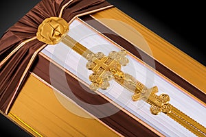 Closed coffin covered with brown and beige cloth decorated with Church gold cross on gray luxury background. Close-up.