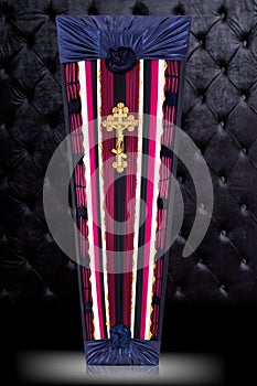 Closed coffin covered with red and white cloth decorated with Church gold cross on gray luxury background.