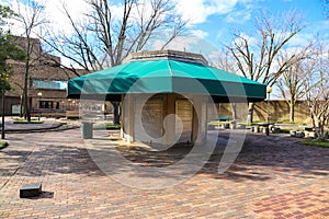 A closed concessions stand with steel doors and a green circular awning in the park surrounded by a red brick footpath photo