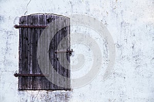 Closed dark brown wooden window with rusted metal hinges on a grungy white grey wall