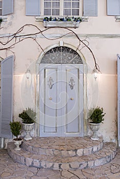 Closed door grey color with a semicircular window on top on an ocher color plastered wall. Town porch with a door and flower