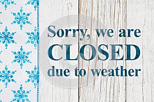 Closed due to weather sign with blue and white snowflakes on with weathered wood