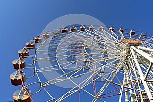 Closed, empty, non-working attraction Ferris wheel with empty booths against a clear blue sky