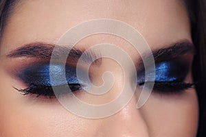 Closed eyes of young beautiful woman with gorgeous trendy facial makeup blue glossy eyelids