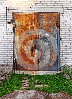 Closed flaps of old metal rusty locked gates in a wall made of white brick and concrete