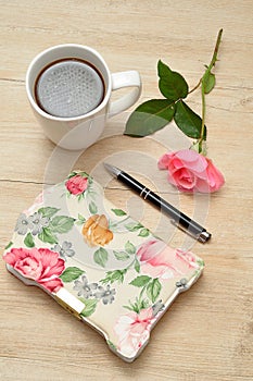 A closed flowery diary on a wooden table with a pink rose