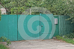 Closed green metal gate and iron door on a wooden fence