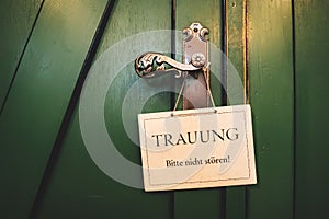 Closed green wooden doors with decorative fittings. On handle hanging white sign `Wedding, please do not disturb