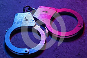 Closed handcuffs on a dark background, illuminated with mixed red and blue light