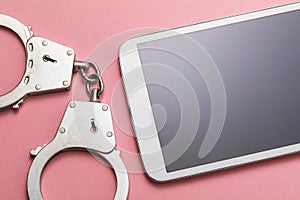 Closed handcuffs and tablet on a pink background. Computer crime concept