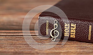 Closed Holy Bible Book with rustic old treble clef note on wooden background