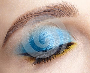 Closed human female eye with blue smoky eyes shadows and yellow liner