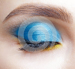 Closed human female eye with blue smoky eyes shadows and yellow liner