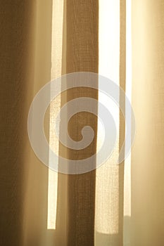 Closed linen curtains hanging on window on a sunny day inside a modern home. Shadow and sunlight shining through cream