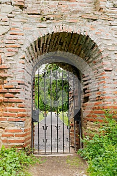 Closed and locked metal iron gate in old brick wall