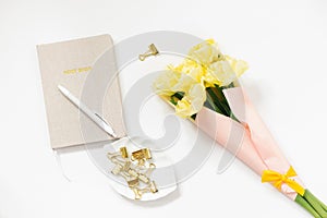 A closed notebook with a beige cover and a pen on it, a bouquet of spring yellow tulips on a white background. Working space in