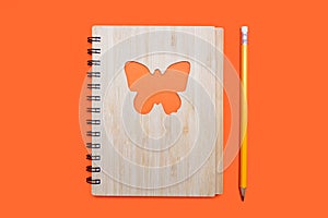 Closed notebook bound in bamboo with a butterfly ornament on an orange background and a yellow pencil