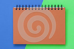 Closed notebook for sketches on spiral, orange cover on the bright colorful background, top view, texture with copy space