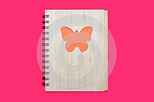 A closed notepad in a babmouk cover with an orange butterfly on a pink background