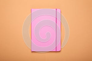 Closed office notebook on pale orange background, top view