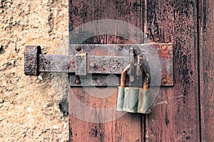 Closed old rusty iron lock and vintage padlock on cracking and peeling weathered red wooden door