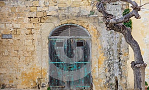 Closed old wooden door on a yellow limestone wall. Mdina, Malta