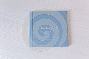 Closed photobook on white wooden table. Blue textile wedding album with silver embossing of Memories