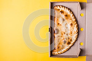 Closed pizza calzone in packing box on yellow background