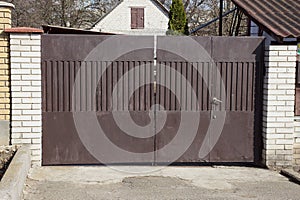 Closed private brown metal gate and part of a brick fence