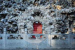 Closed red door in the middle of the porous rock, decorative stone fence from the front
