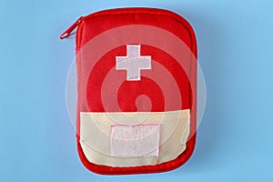 Closed red travel first aid kit pouch on the bright blue background. Photo with a copy space