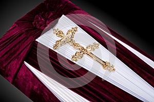 Closed red velvet coffin covered with cloth isolated on gray background. coffin close-up with gold Church cross.