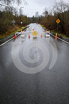 Closed road due to rainfall flooding over the roadway, barricades, empty road, stormy sky