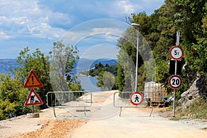 Closed road under construction with various road signs at start of construction site surrounded with protective metal fence