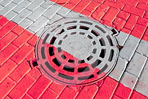 Closed round sewer manhole under red and white road marking