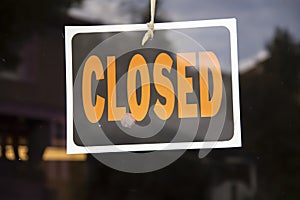 Closed sign hanging in business window by a string - crooked with glob of glue also attaching it to window - some abstract reflect