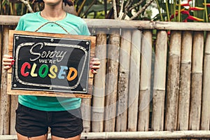 Closed sign wooden board in woman hands. Bali island background.