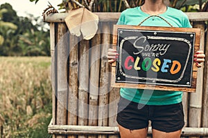 Closed sign wooden board in woman hands. Bali island background.