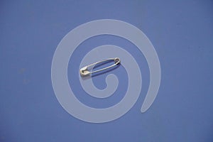 A closed silver safety pin isolated on a blue background. Also known as shield pin, lingerie pin, clasp, diaper pin, fastener and