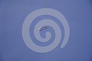 A closed silver safety pin isolated on a blue background. Also known as shield pin, lingerie pin, clasp, diaper pin, fastener and