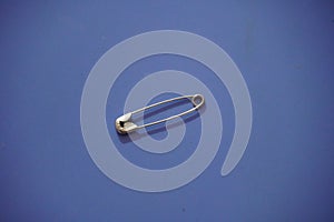 A closed silver safety pin isolated on a blue background. Also known as shield pin, lingerie pin, clasp, diaper pin, fastener and