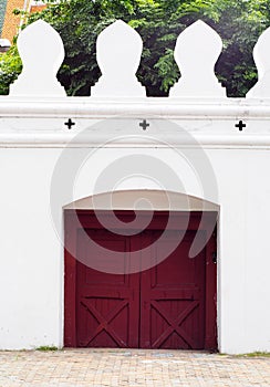 Closed small exit wooden red brown gate door on the massive wall of the THAI GRAND PALACE