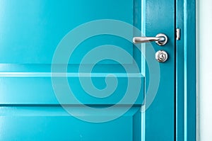 Closed solid wooden door is painted in bright blue with a beautiful metal handle and lock