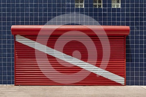Closed store shutter painted to red scuba diving flag with a wall covered with blue tiles