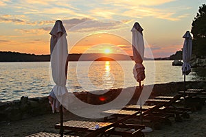 Closed sunshades and deck chairs on the seaside promenade of Rab City, in sunset light. Croatia.