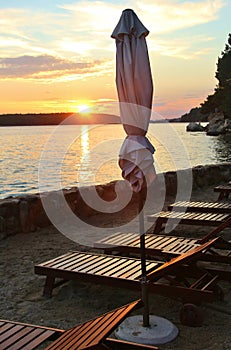 Closed sunshades and deck chairs on the seaside promenade of Rab City, in sunset light. Croatia.