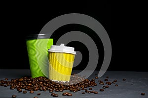 Closed take-out coffee with cup holder. Two yellow and green cups with coffee beans over black background.