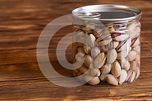 A closed transparent jar of toasted salted pistachios sits on a vintage rustic pine-board table